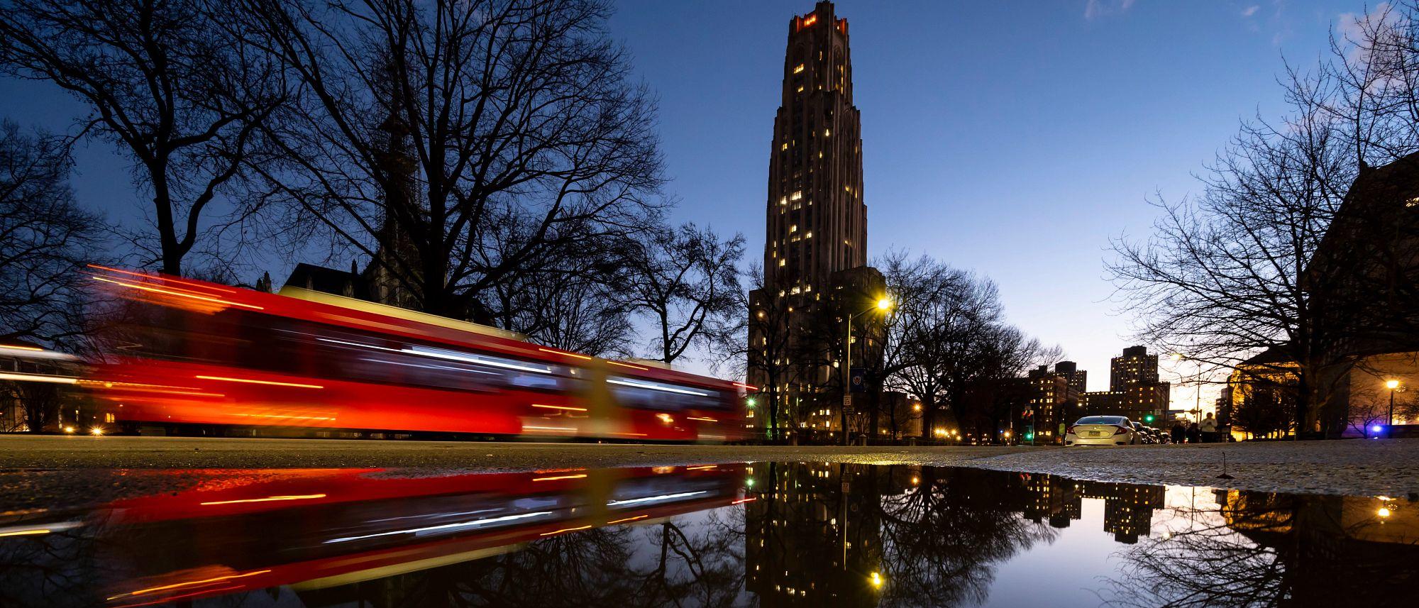 A citybus zooming past the Cathedral of Learning at night